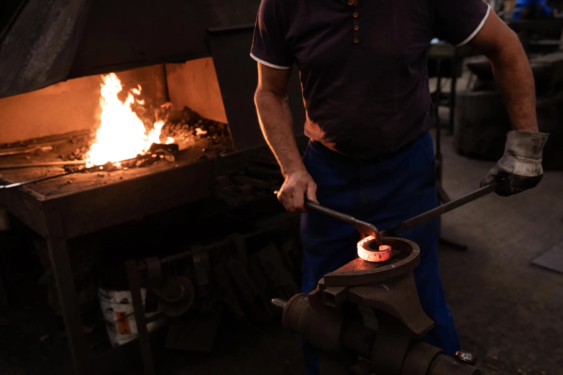 Un artisan façonne une volute de fer chauffée à la forge, sur une enclume.